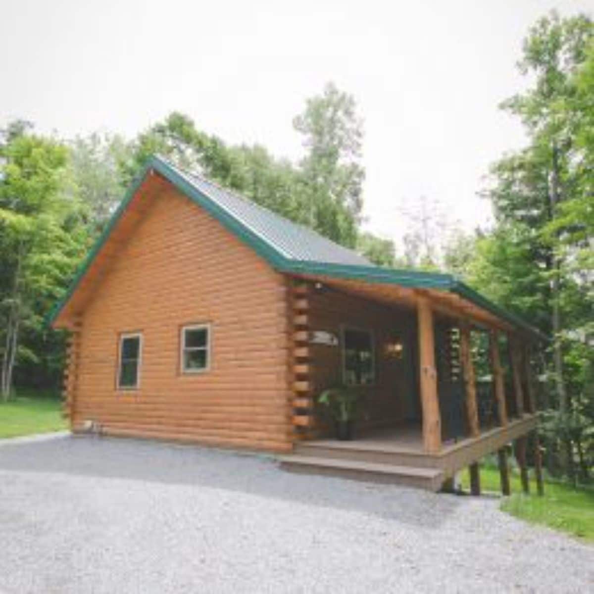 side of log cabin with green roof and covered porch