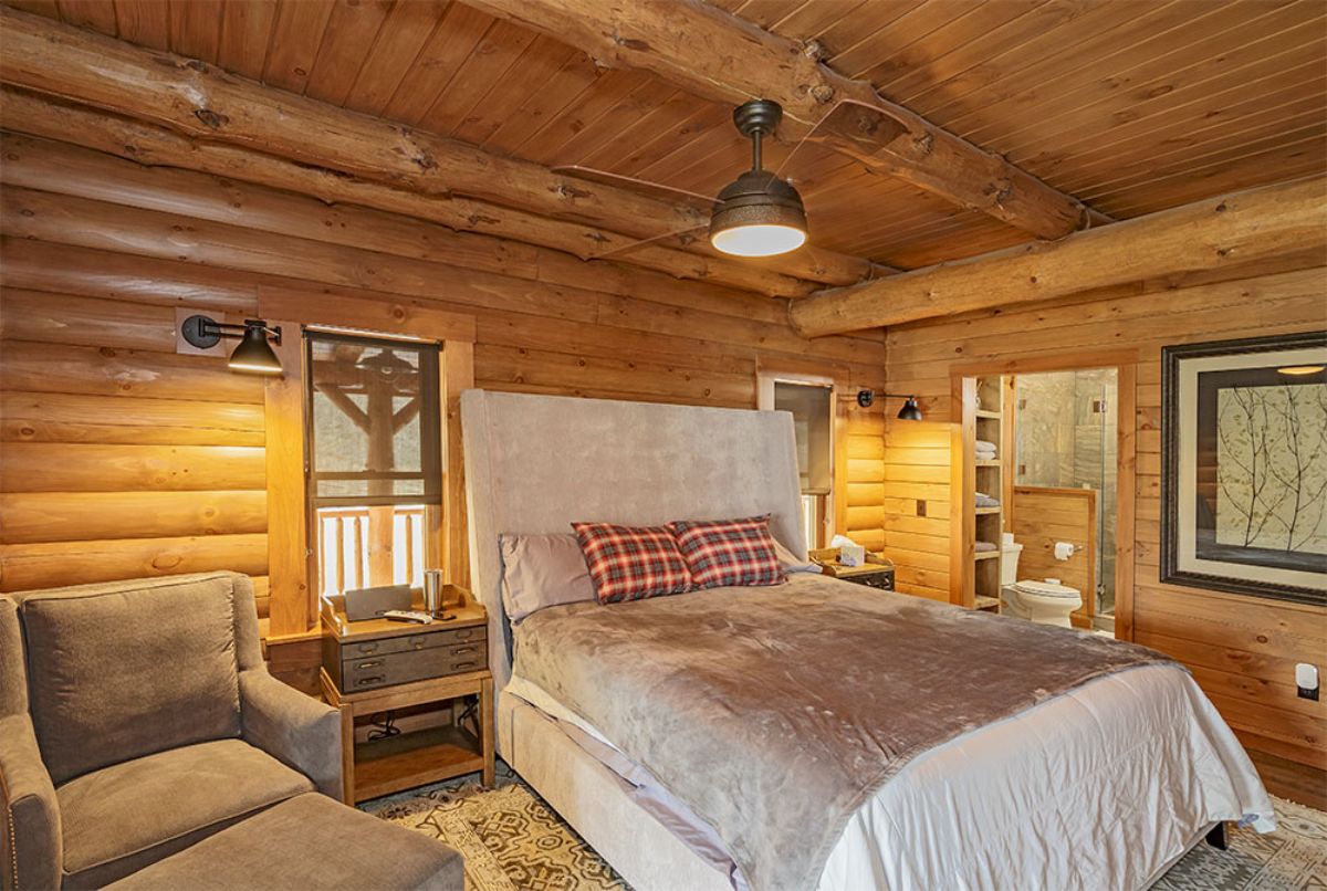 white bedding on bed in log cabin bedroom with light brown sofa on left