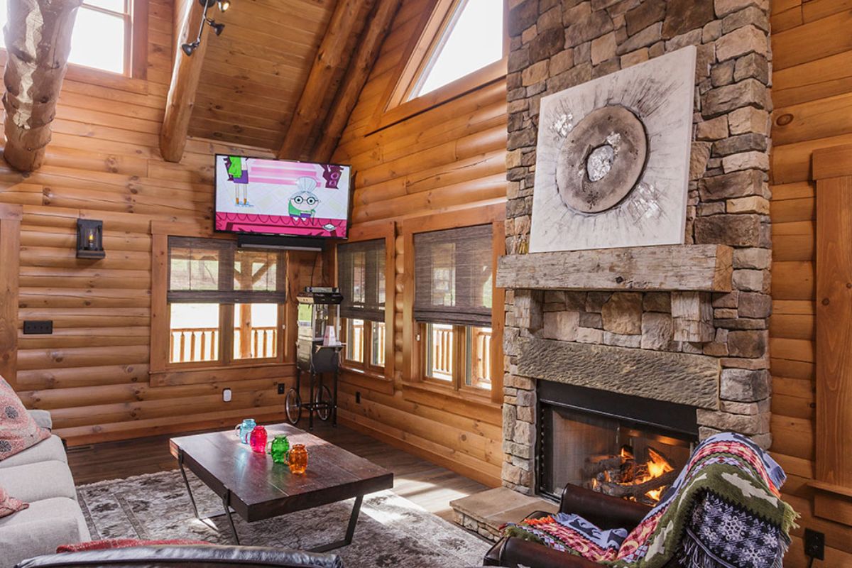stone fireplace in foreground with windows on walls of log cabin walls