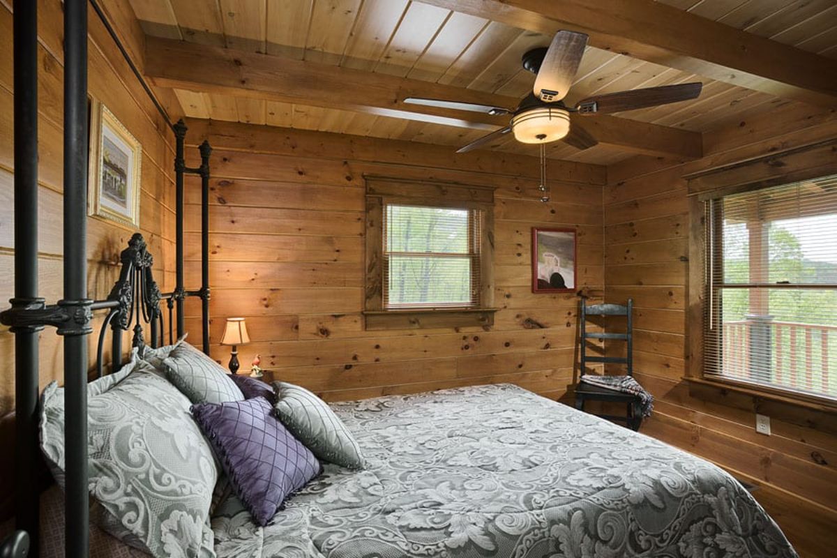 bed with light bedding against log cabin wall with ceiling fan above bed