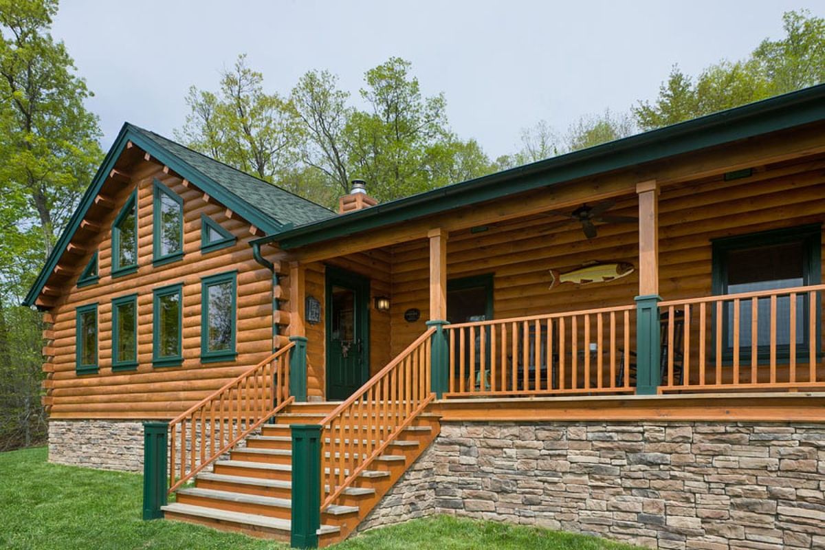 front of log cabin with stone foundation and green trim around porch and windows