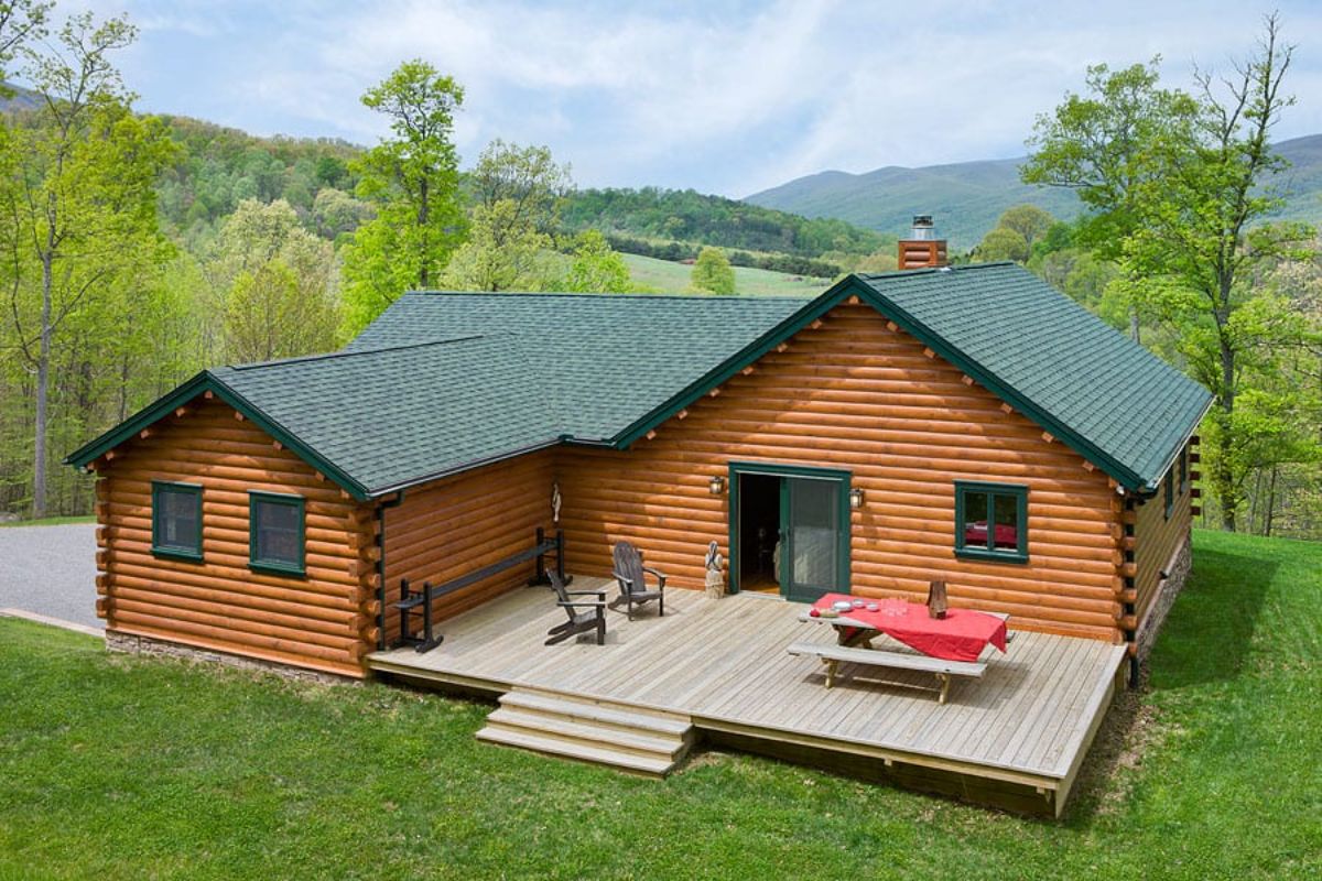 log cabin on hill with green roof and large open deck off back of home