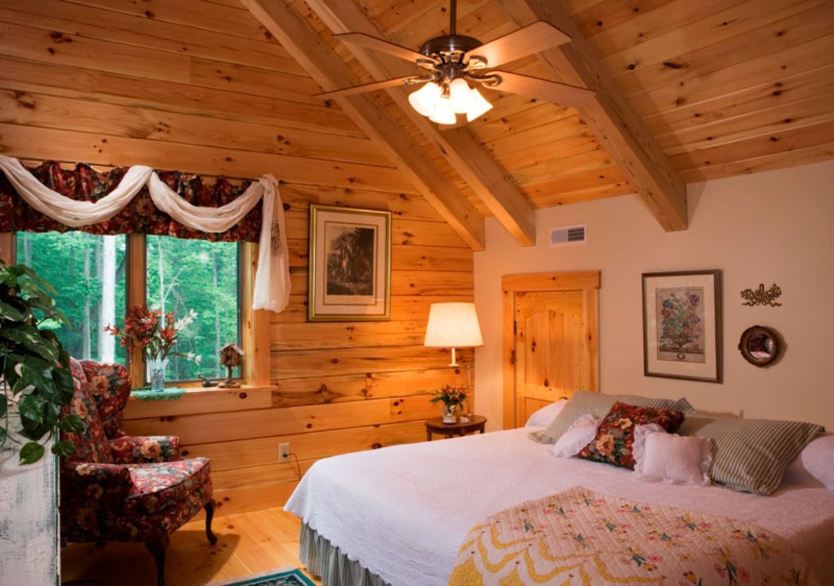 white and pink bedding on bed in lofted bedroom of log cabin with red and white curtains