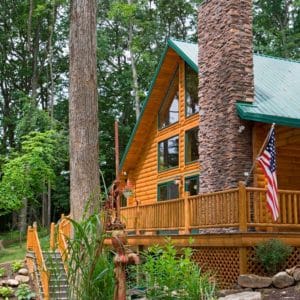 front porch of light wood log cabin with green roof