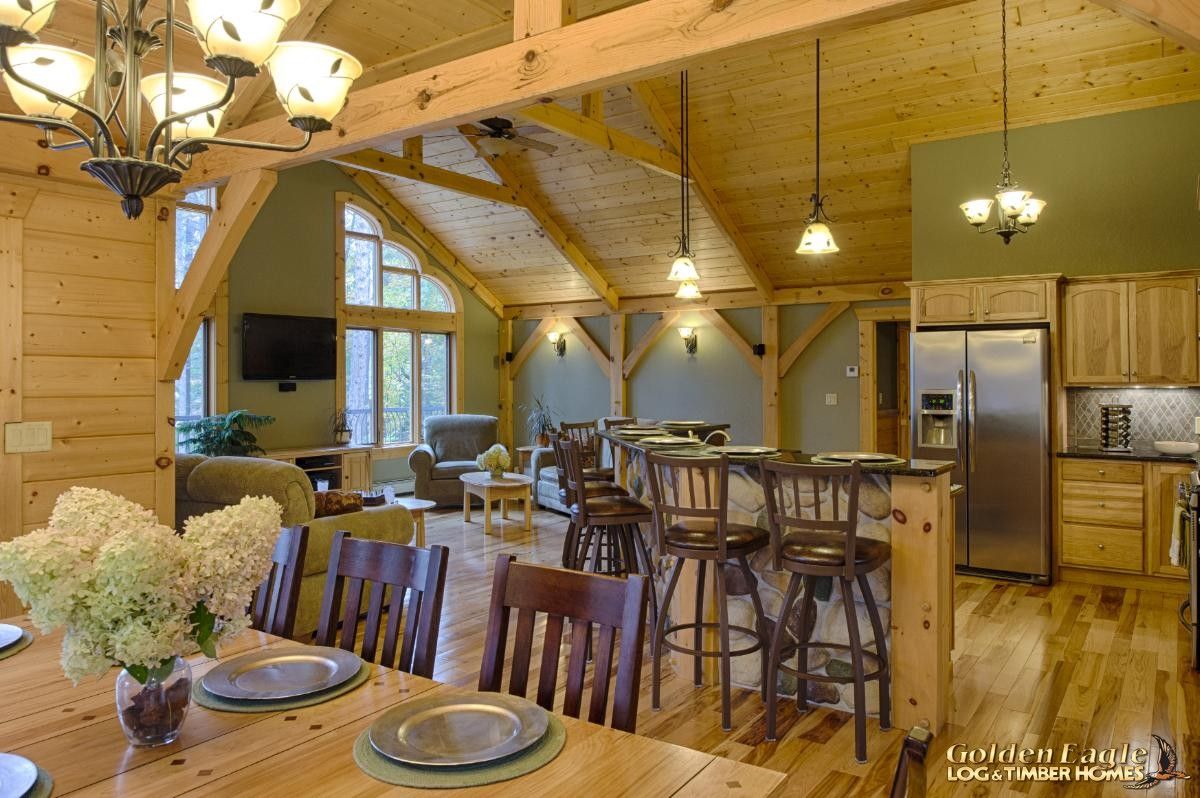 view over dining table to bar on edge of kitchen in light wood interior of log cabin