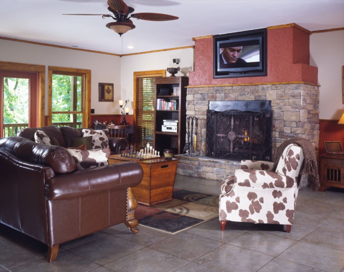 brown leather sofa in front of stone fireplace with cow print white and brown chair beside it