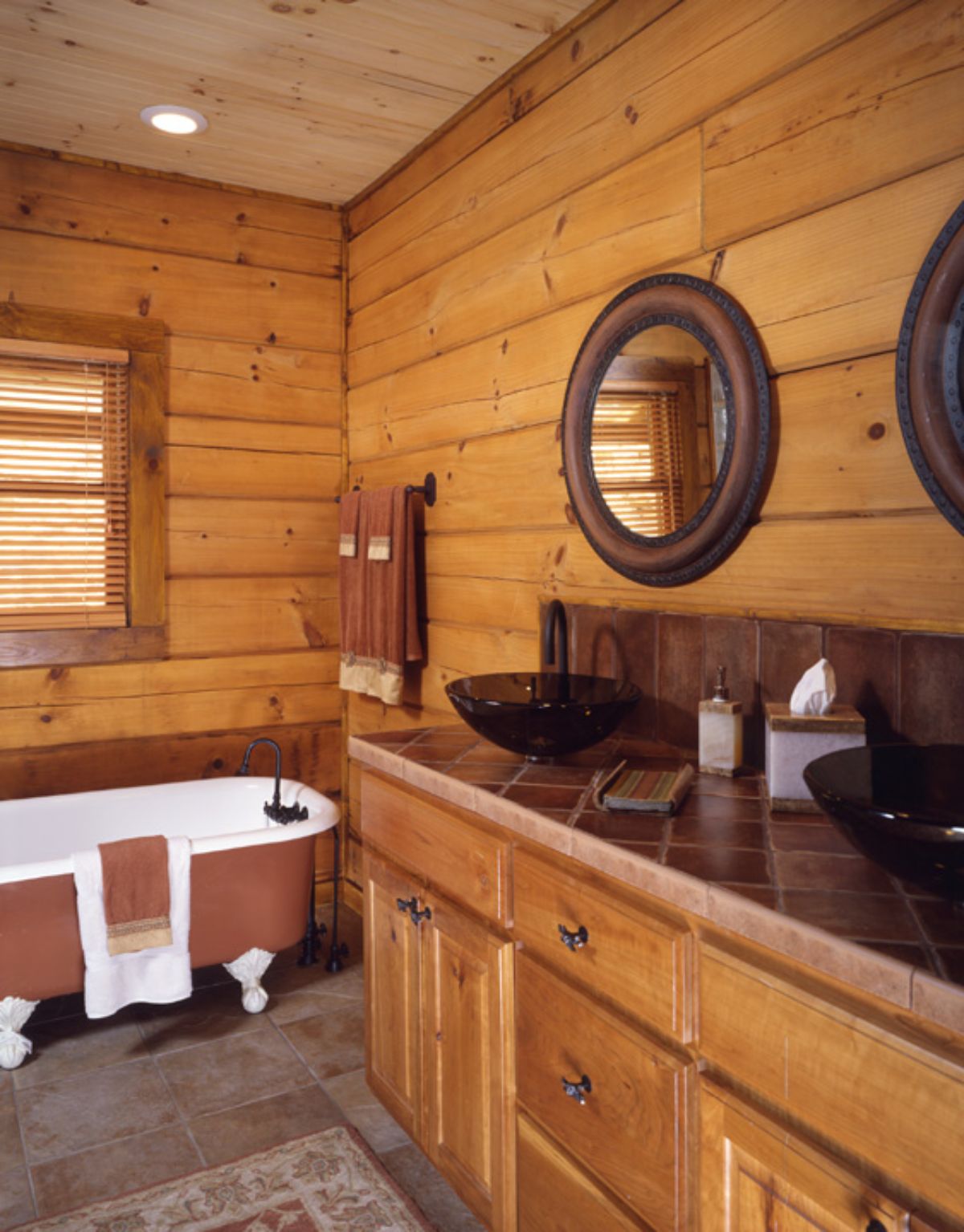 white and brown clawfoot bathtub in log bathroom with bowl sinks on top of wood cabinet