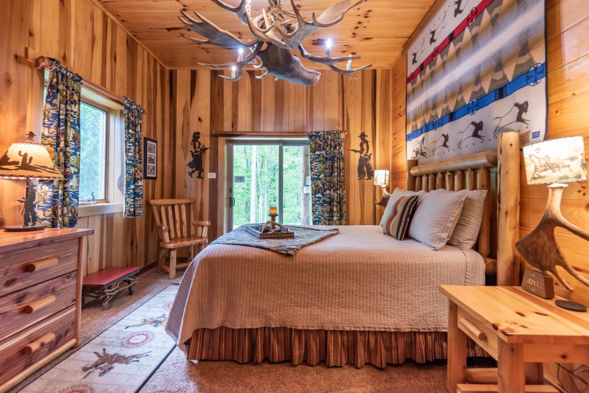 cream bedding on bed in log cabin with wall of rustic cloth behind headboard