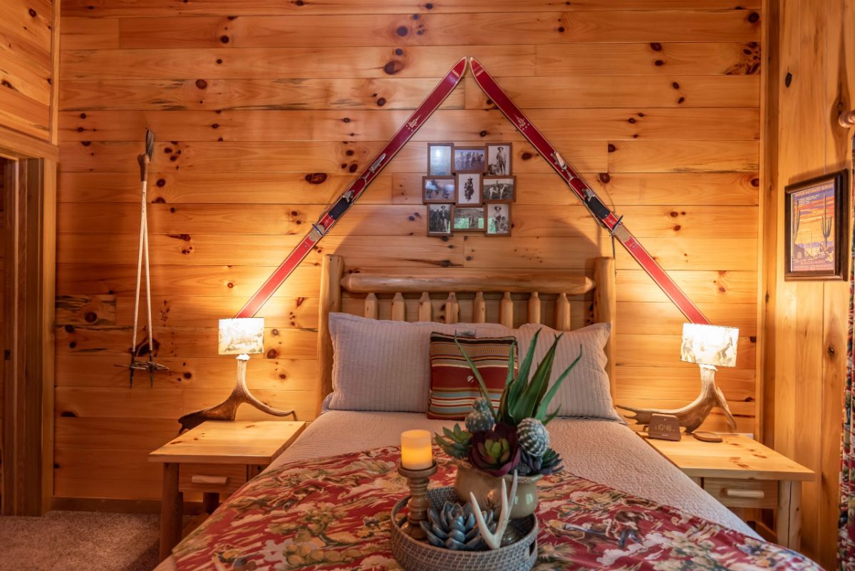 bed against log cabin wall with log headboard and snow skis at an triangular angle behind headboard