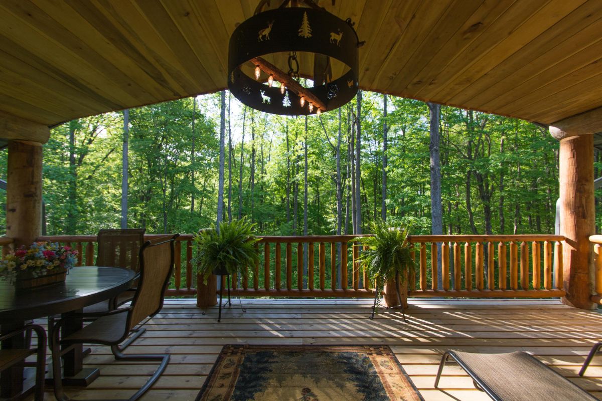 porch on log cabin with wood railing and chandelier above middle of porch