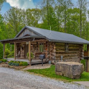 rustic log cabin with covered porch against rock driveway