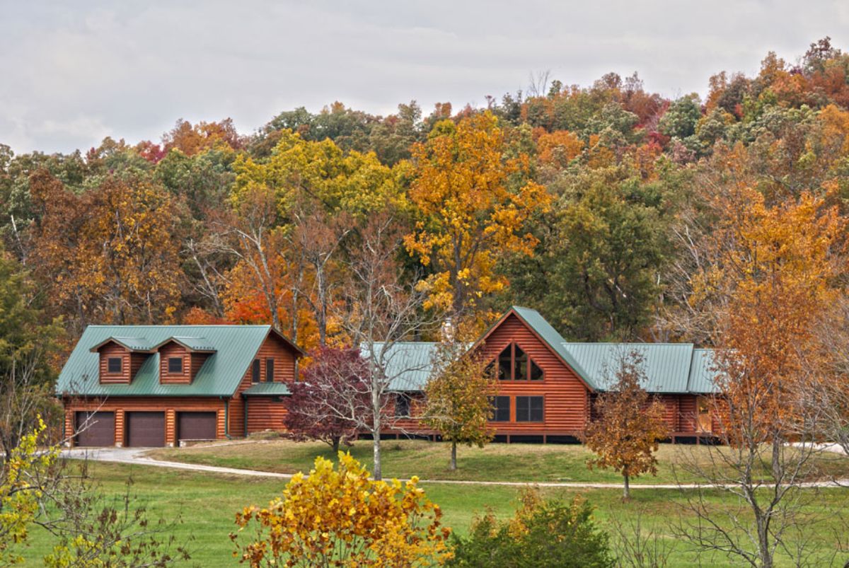 log cabin with light green roof against fall leaves on trees background