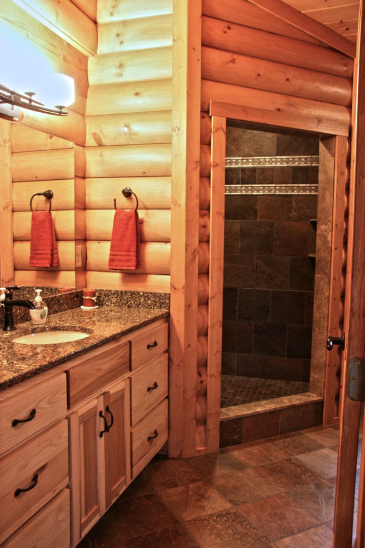 glass door n corner shower in log cabin bathroom with white sink in dark granite counter