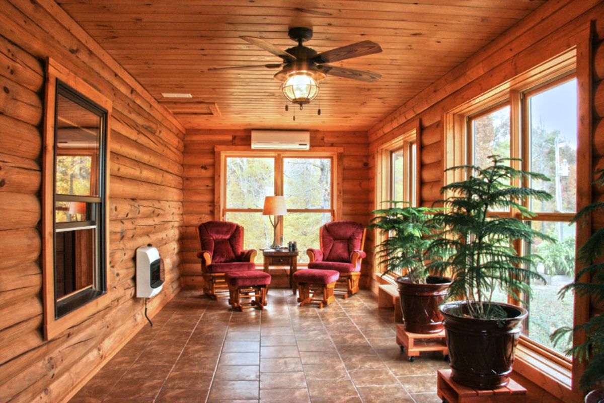 four seasons room of log cabin with windows on right wall and ceiling fan above