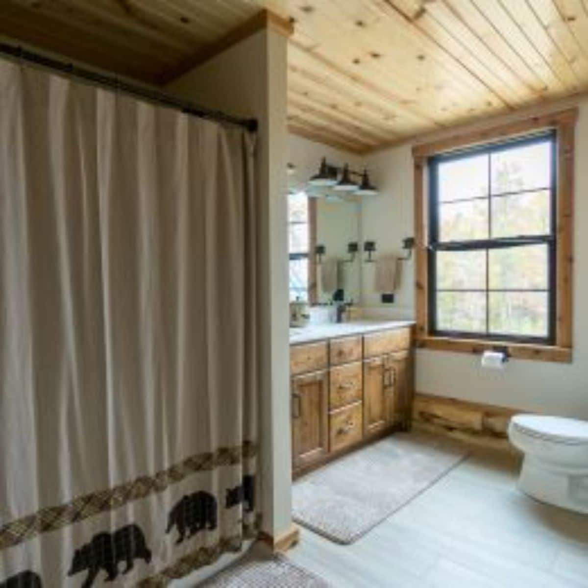 rustic shower curtain with bears on bottom on shower on left of image with toilet on right