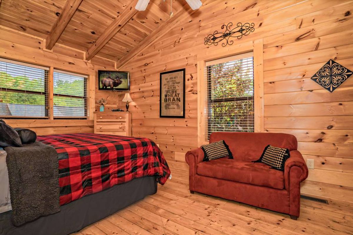 maroon sofa against wall in bedroom with red and black bedding on log cabin bed