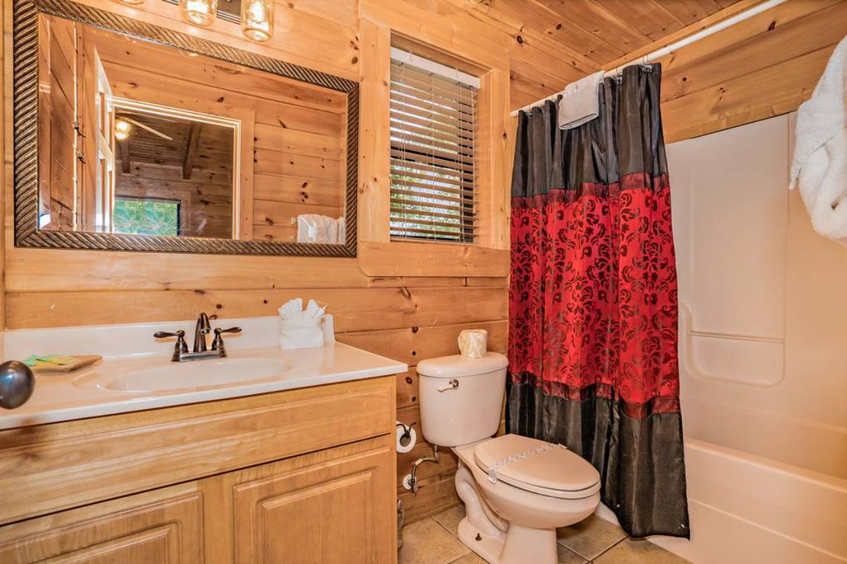black and red shower curtain in bathroom with light wood cabinet and white toilet
