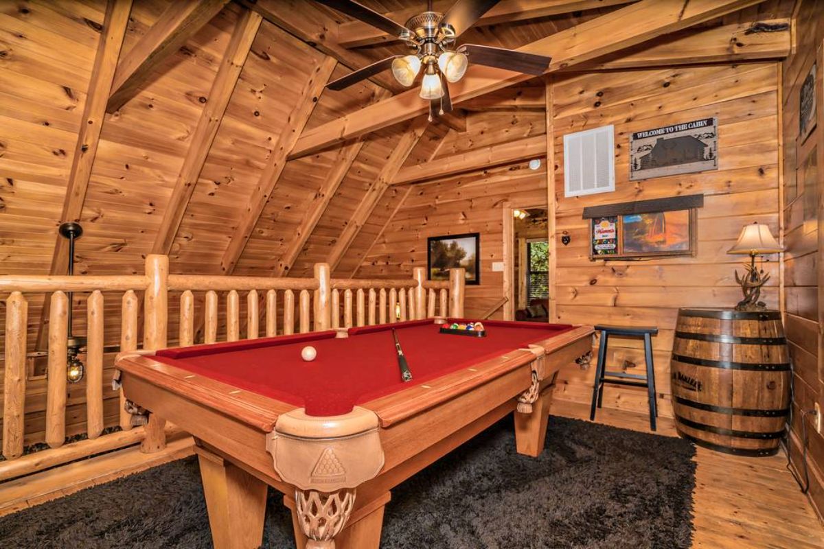 red felt top on light wood pool table with black carpet beneath in log cabin