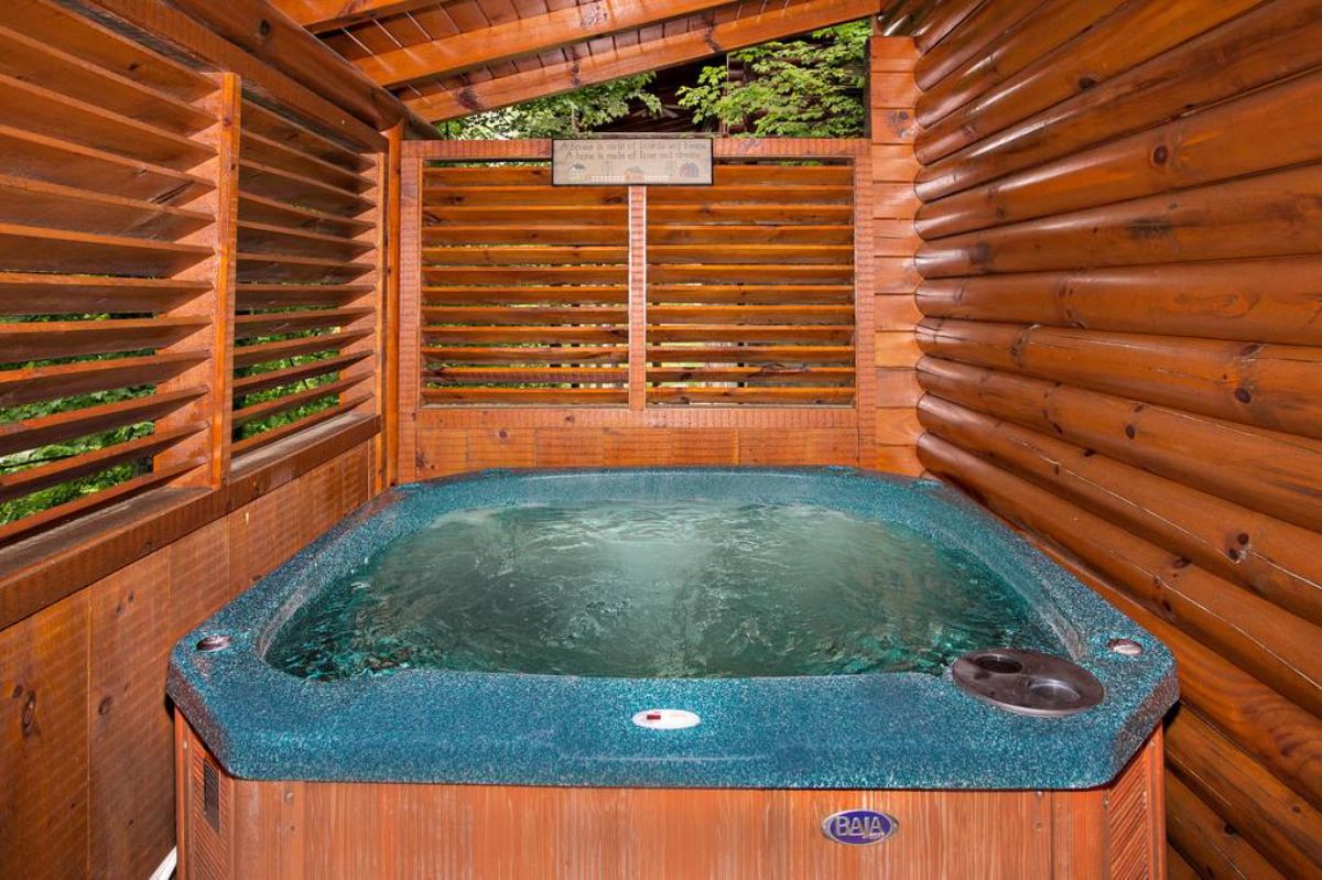blue hot tub with wood slat surround and walls behind log cabin