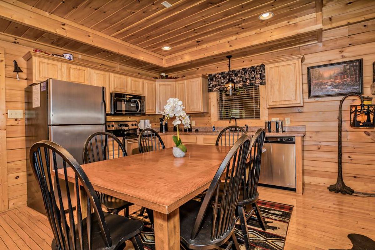 wood dining table with dark wood chairs and kitchen with stainless steel appliances in background