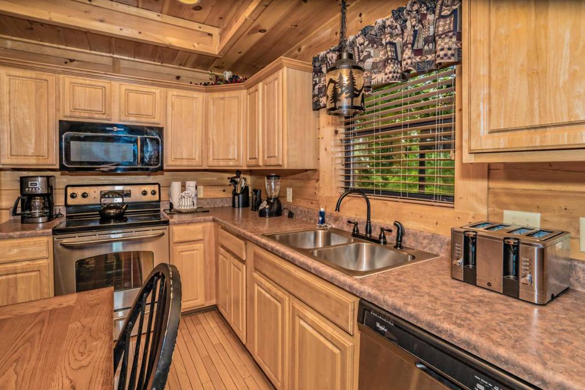 light wood cabinets with stainless steel appliances in kitchen with floral curtain above kitchen sink window