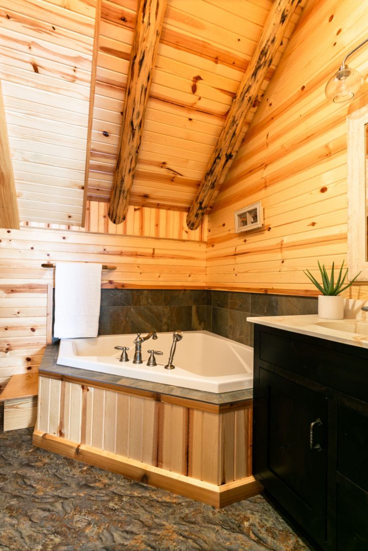 soaking tub in corner of log cabin bathroom with gray stone background and black vanity