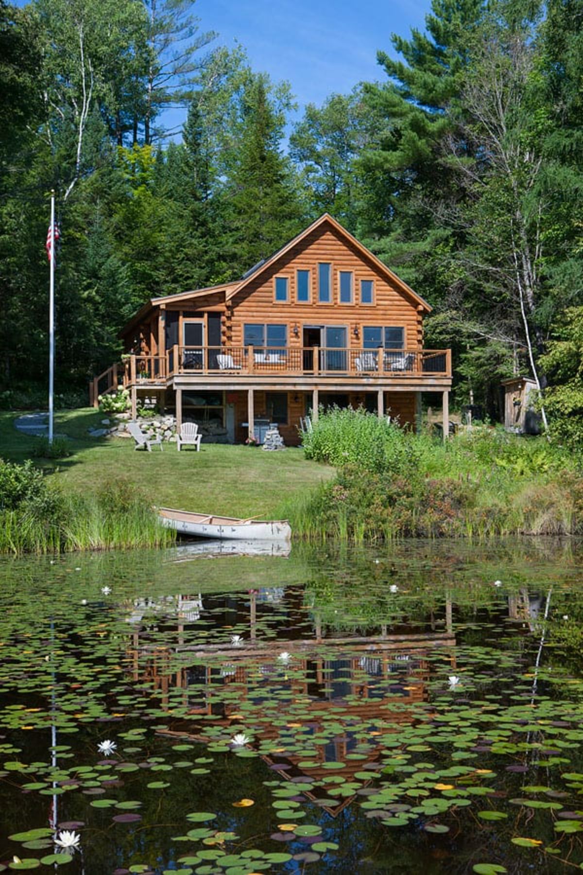 log cabin on hill above pond with small boat in edge of pond