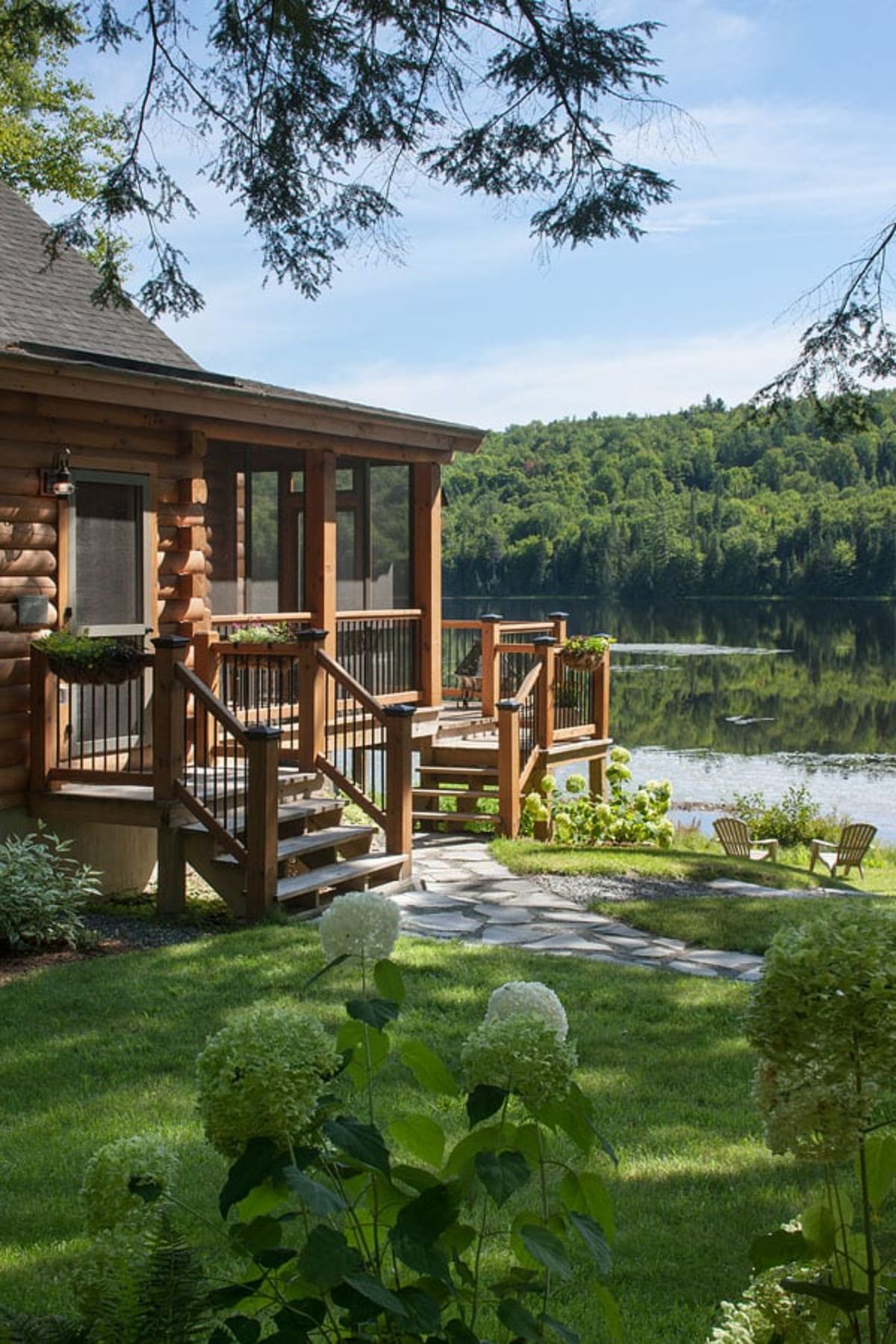 small porch on side of log cabin with stone walkway overlooking pond in background