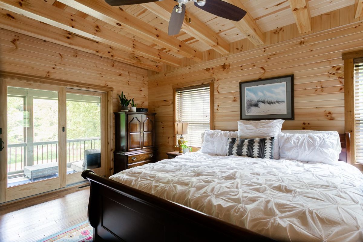 dark wood sleigh bed with white bedding in light wood log cabin bedroom