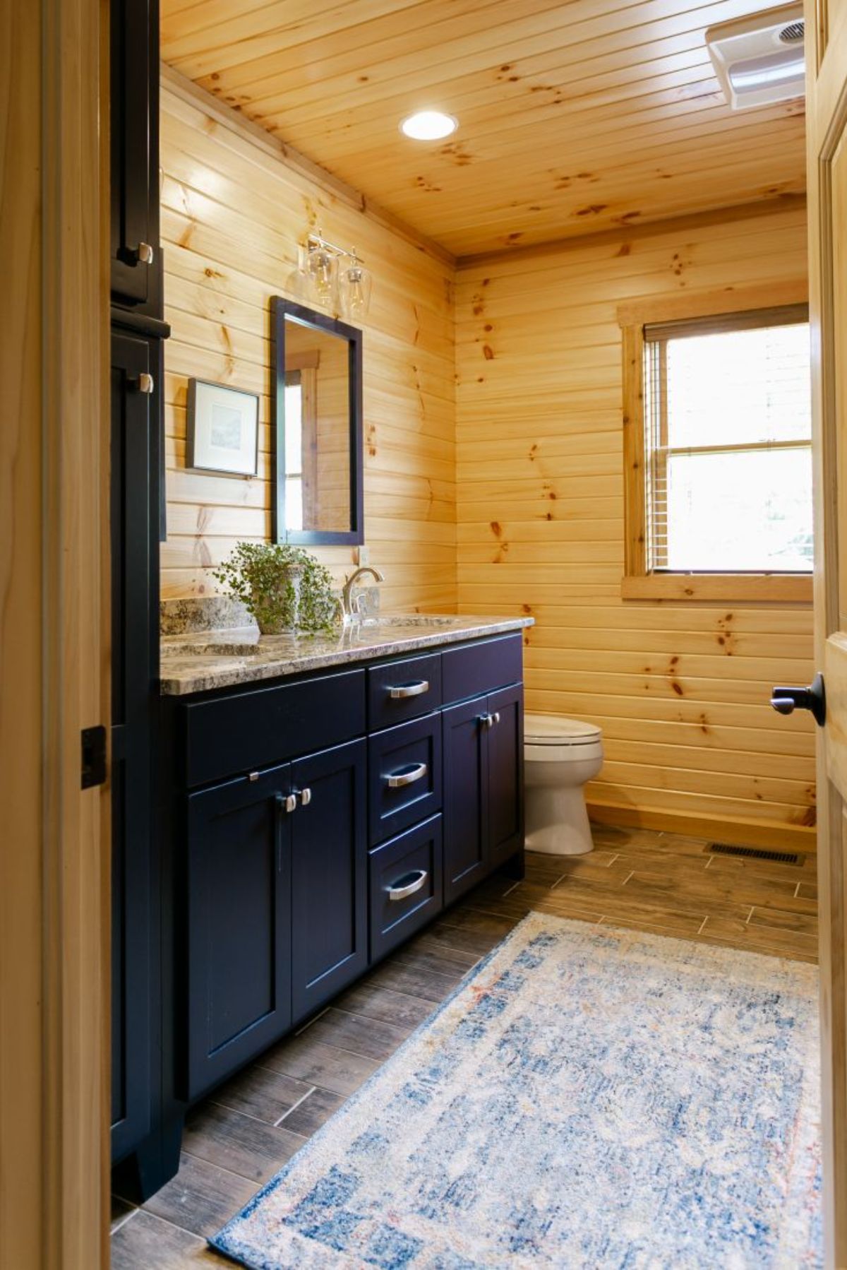blue wood cabinet in bathroom with light white rug and light wood walls