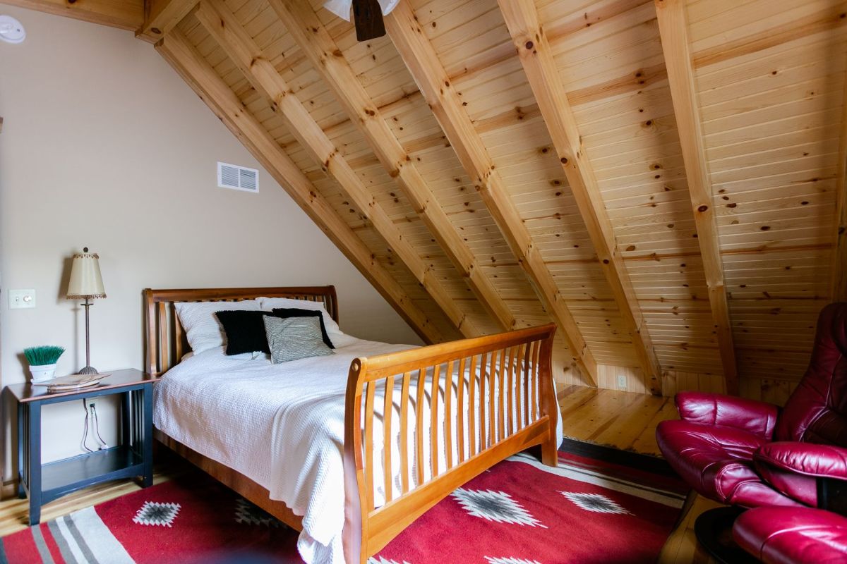 light wood bed frame with white bedding over red and blue rug in log cabin loft