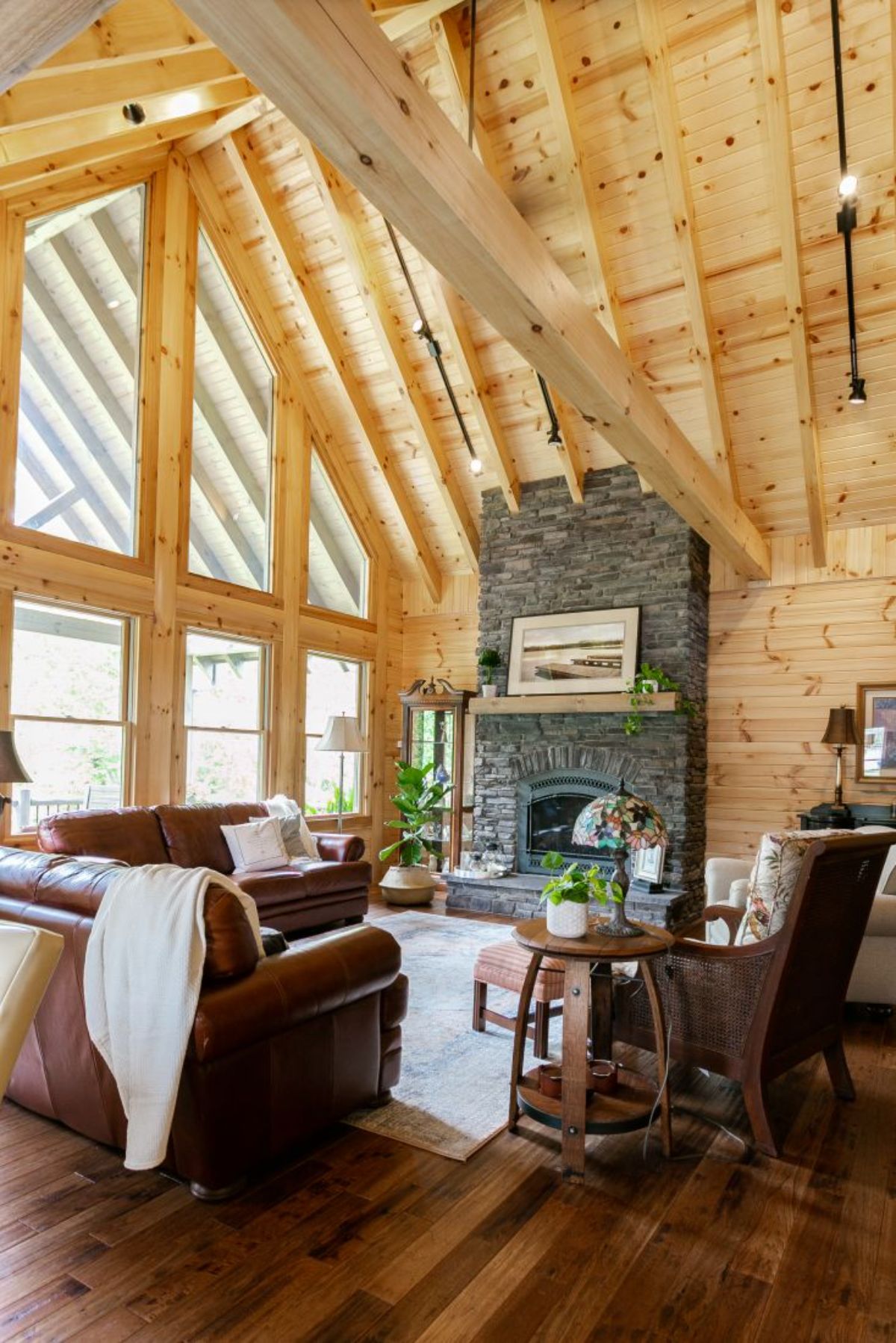 dark brown leather sofa in front of stone fireplace against wall of windows