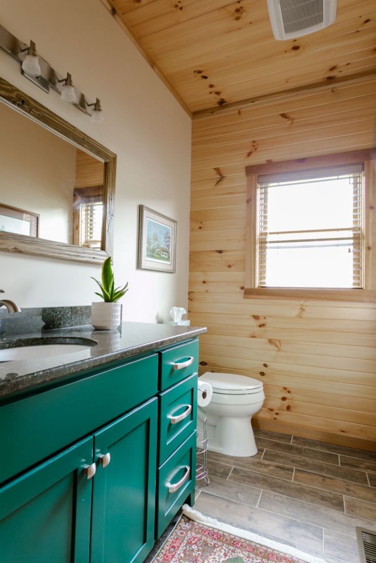 bright teal vanity with gray counters and white sink next to white toilet in bathroom with light wood walls