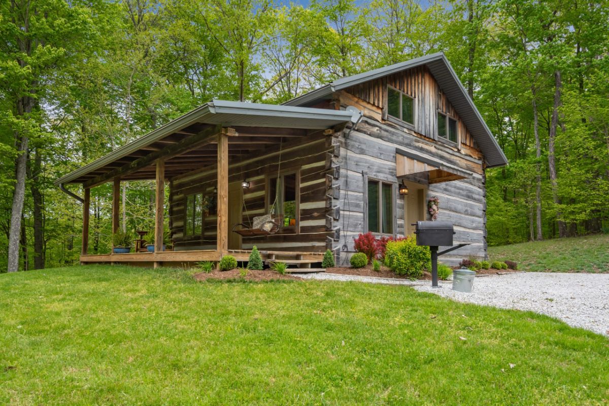 rustic  log cabin at end of gravel driveway with shrubs by side of home