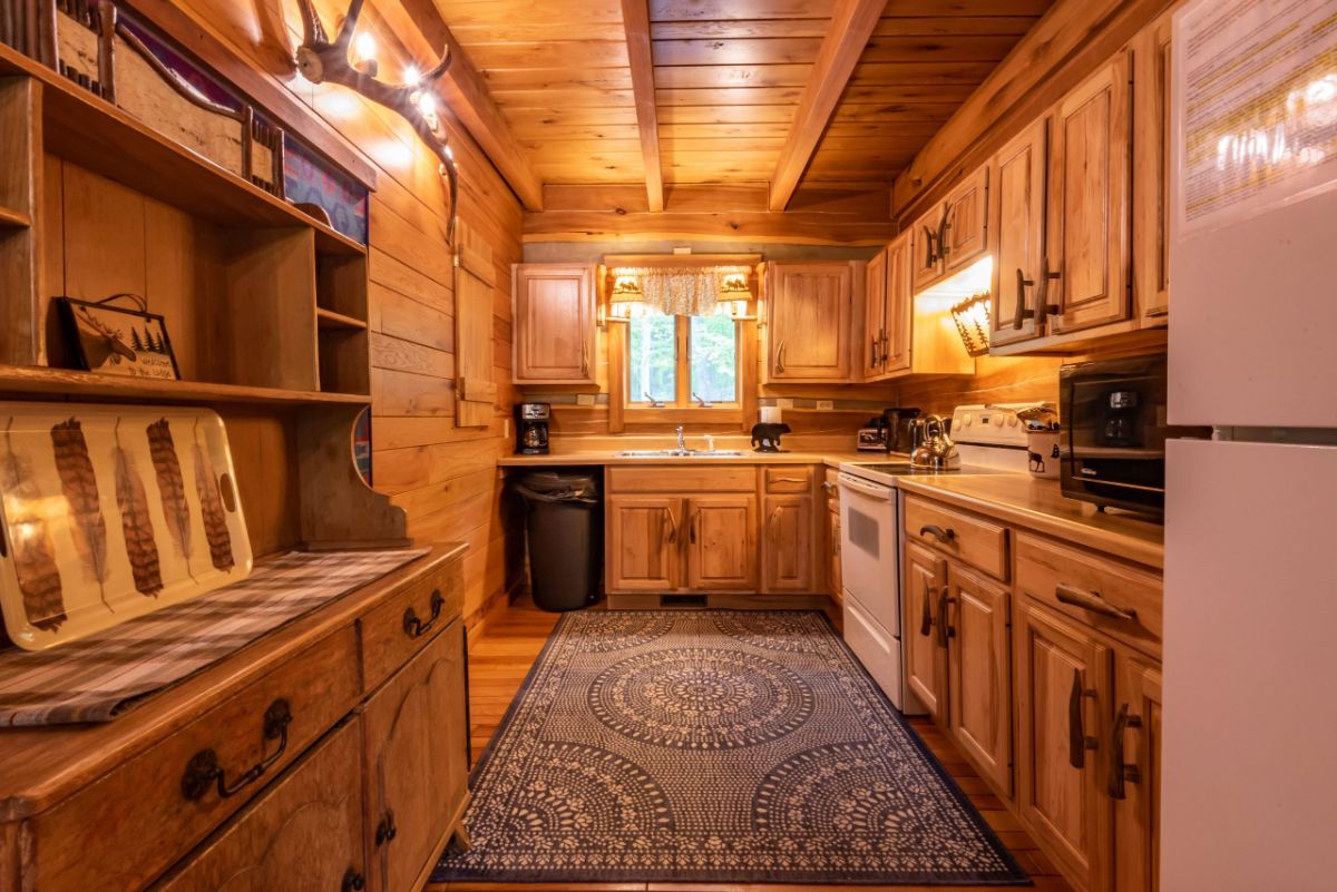 kitchen in log cabin with long blue rug in middle of space and window above sink at end of room