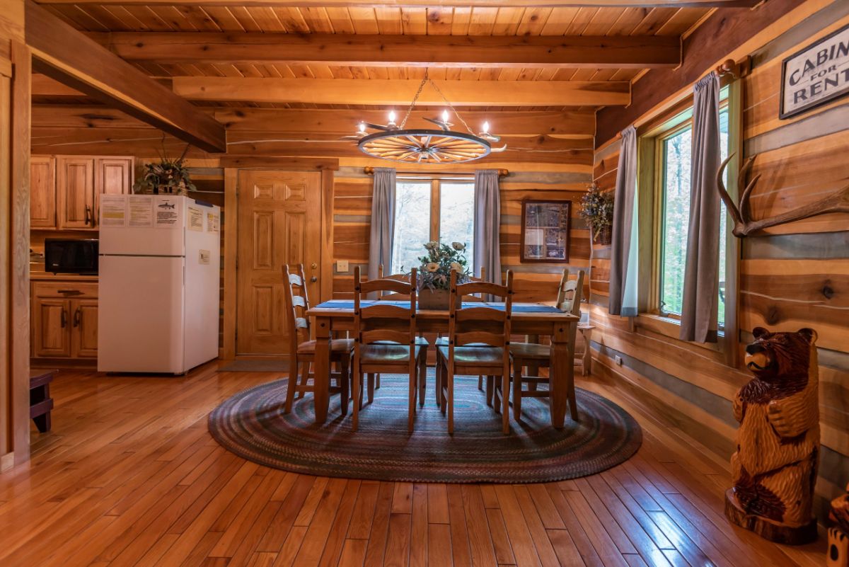 dining table sitting over oval rug against windows in log cabin