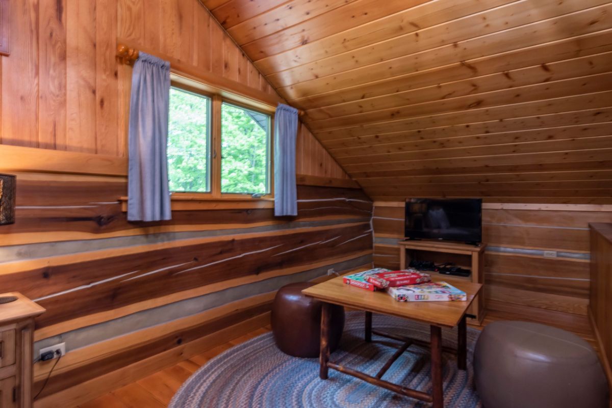 table with ottoman in front of television in corner of log cabin loft bedroom