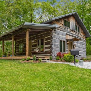 rustic log cabin at end of gravel driveway with shrubs by side of home