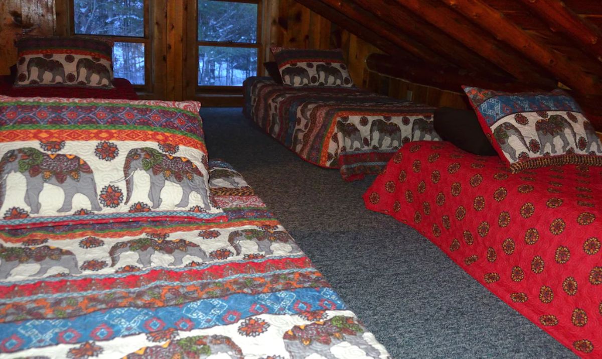 loft with twin beds lined up with rustic bedding and windows against far wall