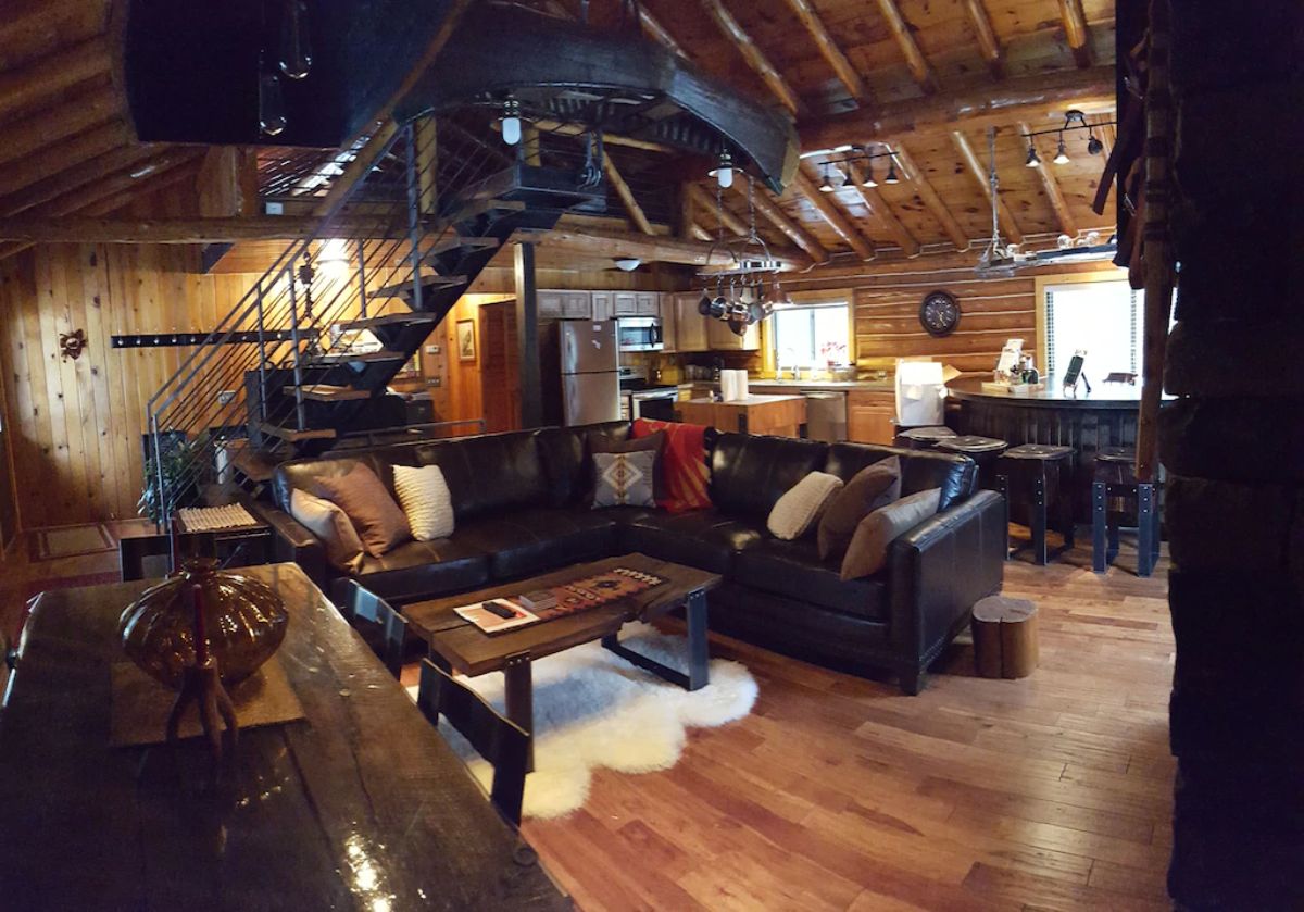 living area of log cabin with black leather sofa and wood coffee table over white rug