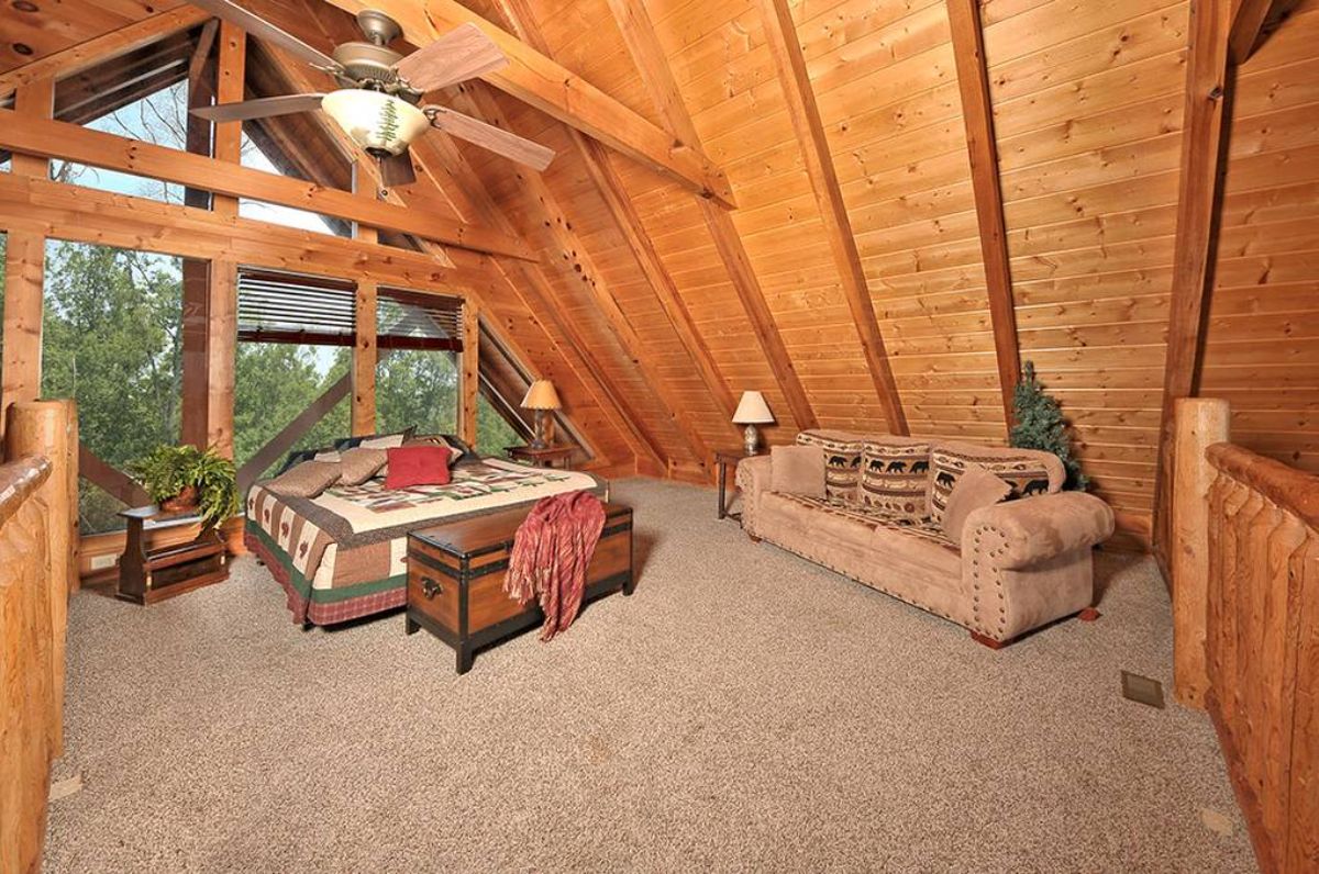 light brown sofa under eaves of log cabin with bed in front of windows