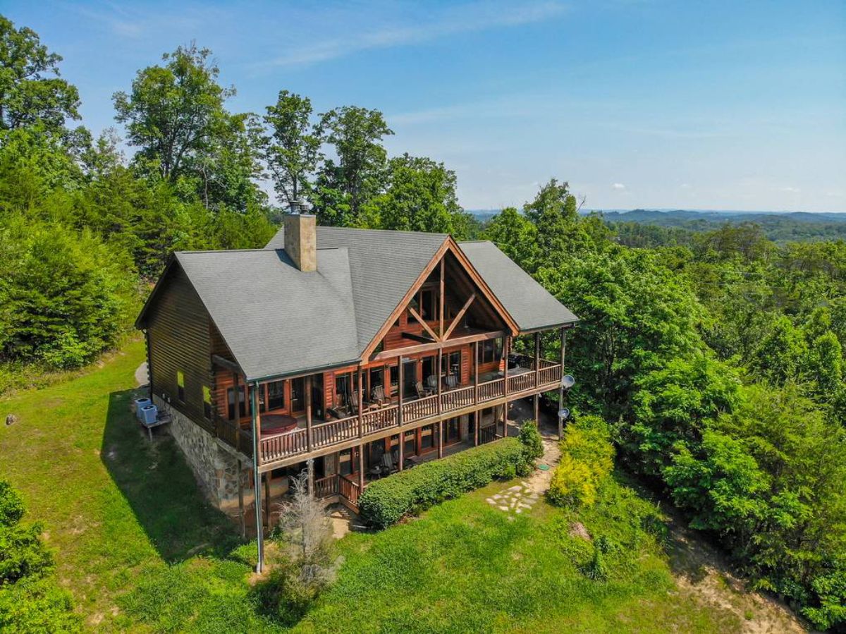 large log cabin with two stories and wrap around covered porches with trees in background