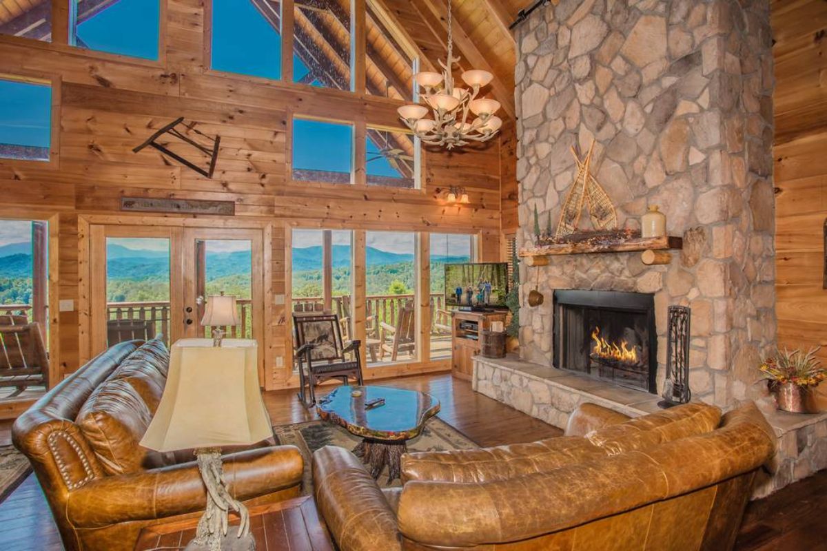 brown leather sofa in foreground with stone fireplace on right side of images