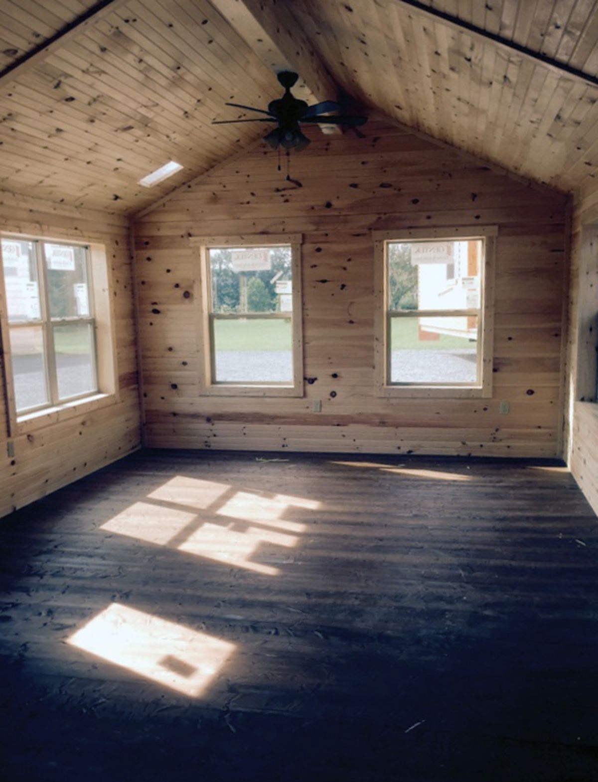 end of log cabin living space with windows on end of wall and dark wood floor