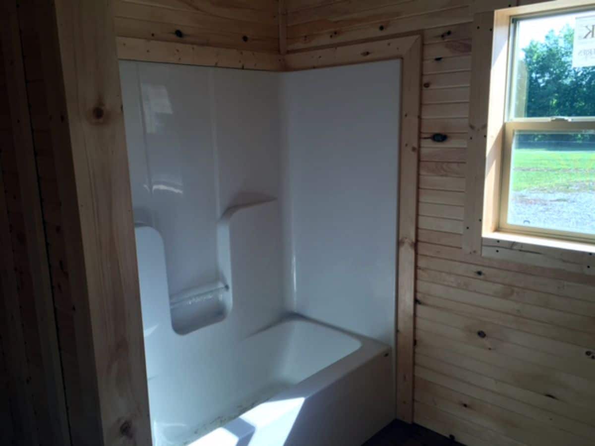 bathtub shower combination in log cabin bathroom with window next to bath