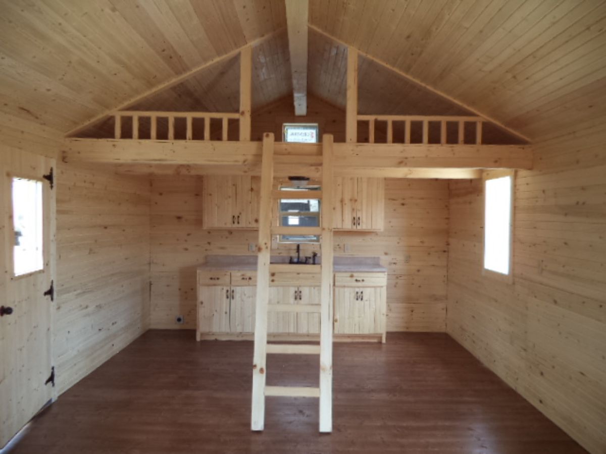 ladder to loft in log cabin with kitchen in background