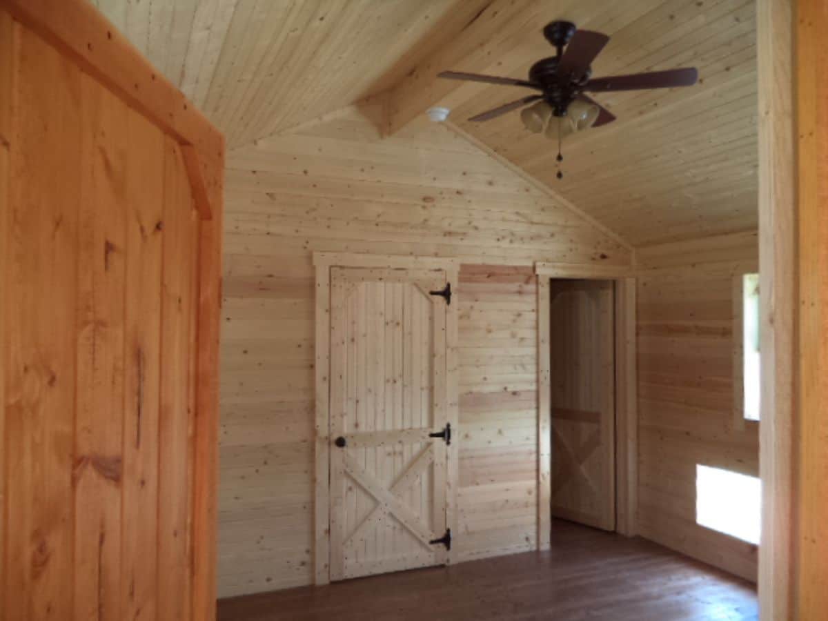 bedroom in log cabin with ceiling fan and door open on right side