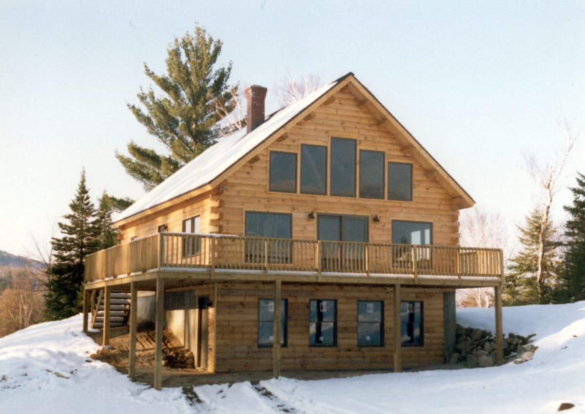 back of log cabin with wall of windows behind open deck
