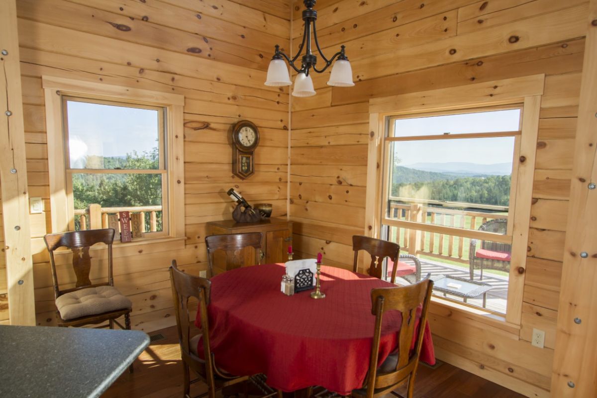 table with red tablecloth against wall by windows in log cabin