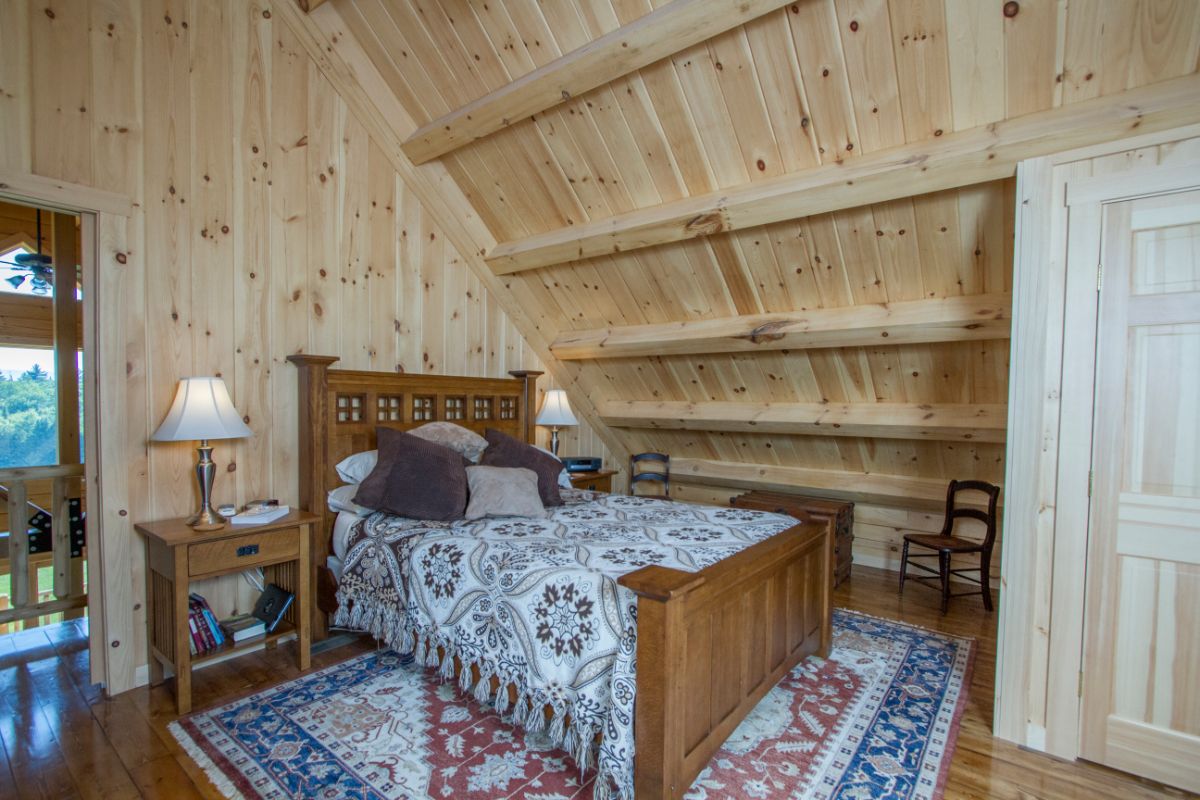 wood bed frame with blue and white blanket underneath eaves of loft